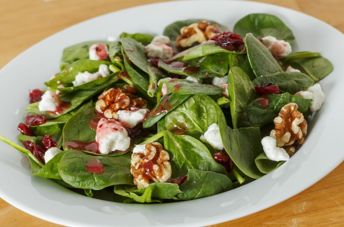 Spinach Salad with Goat Cheese and Walnuts On A White Serving Plate