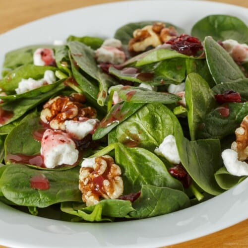 Spinach Salad with Goat Cheese and Walnuts On A White Serving Plate